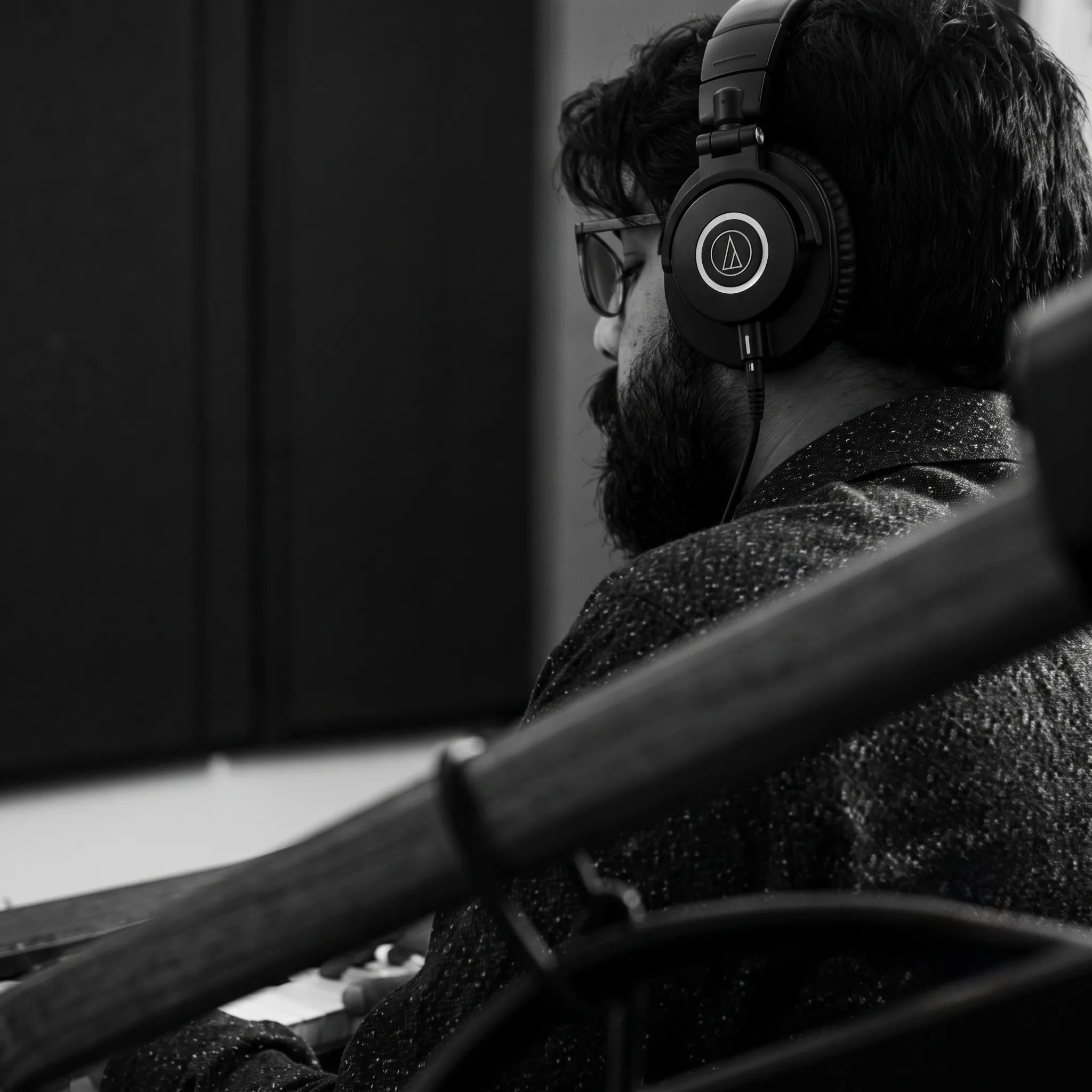 Khandaker Rahin in the studio, wearing glasses and headphones, seen in profile behind a microphone arm (black and white).