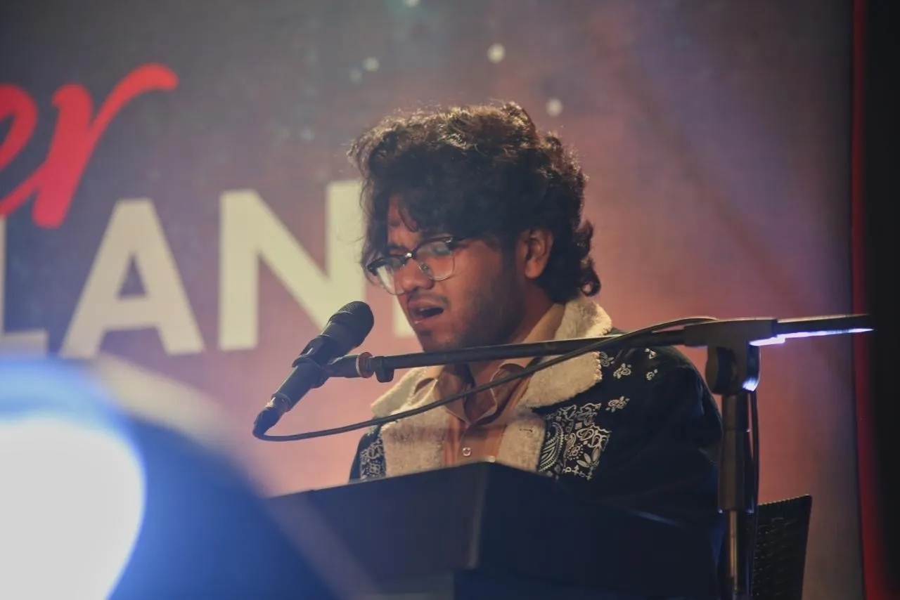 Kazi Munif Ahmed performing on stage at a keyboard, singing into a microphone.